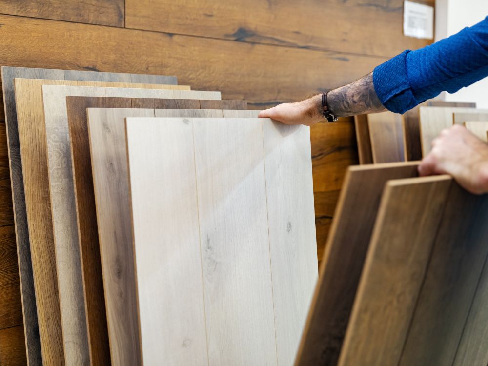 Pessoa escolhendo modelos de piso laminado em loja de revestimentos, avaliando opções estéticas e funcionais para uso comercial.