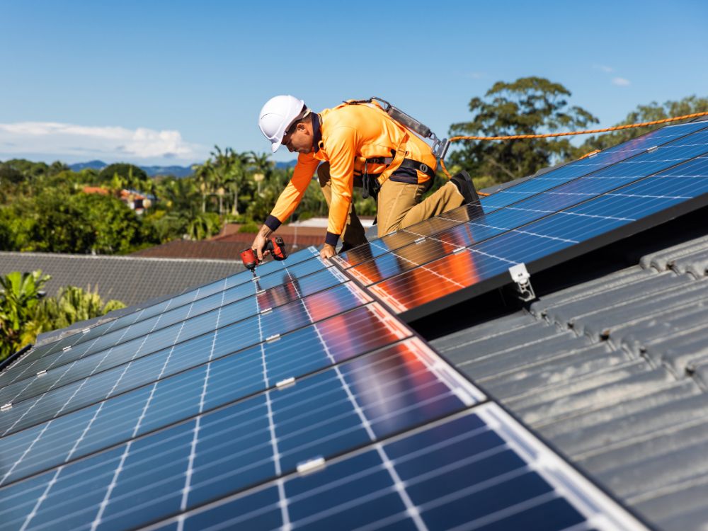 Instalação de painéis solares em telhado residencial, com técnico utilizando equipamentos de segurança durante a montagem do sistema de energia solar.