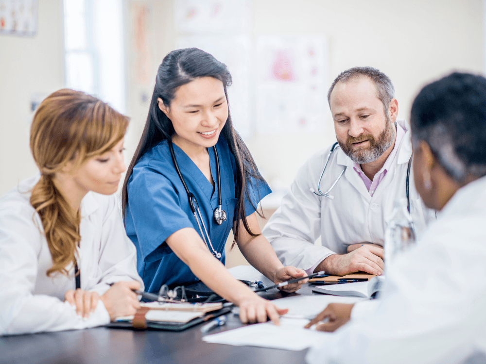 Grupo de médicos conversando, enquanto um deles aponta para prontuário em cima da mesa